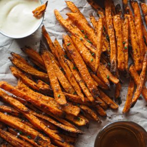 Crispy Baked Sweet Potato Fries with Spicy Mayo, the perfect fall appetizer, side dish, game-day snack, it all works. The cool thing is that they’re healthier than if fried, super easy to make and are actually crispy! There's a small bowl with red pepper flakes at the top, a metallic bowl with the spicy mayo and a dipped sweet potato on the left and a glass with beer at the bottom. In the centre and diagonally the sweet potatoes are laying.