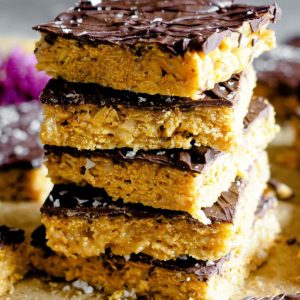 Healthy-ish Cornflakes and Nut Butter Bars, naturally gluten-free and vegan. They are easy and simple to make, and with that chocolate top, they are just the perfect snack. This is a 30 degree angle shot of the bars layering one on top of each other. The gooey crunchy cornflakes, chocolate and flaky sea salt can be clearly distinguished.