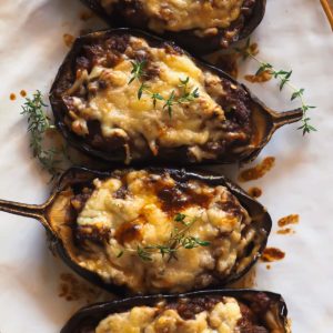 This Sausage Stuffed Aubergine recipe makes a delicious, hearty and wholesome main that everybody will love (no aubergine fans included)! Roasted aubergine is combined with a heavenly tomato sauce, made even better with the addition of sausage and topped with mature cheddar cheese. Overhead close shot of the aubergine served on a white plate and garnished with thyme.