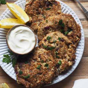 These Tuna Cakes (Tuna Burgers) are delicious, flavourful and a life-savior weeknight dinner – they’re also gluten-free. They are made out of pantry staples and are also perfect for meal prep! This image is an overhead shot of ta plat with the tuna burgers overlapping each other disposed in a semi circle. There's a mayo dip on the left, a few wedges as well on the left hand side, a teaspoon with mayo on the top right corner and a kitchen towel on the bottom right corner.