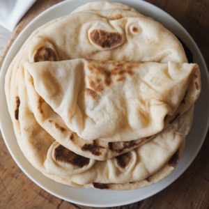 This delicious, pillowy soft Turkish Flatbread is simply incredible! It’s extra soft, tender and hollow, a perfect cross between Naan bread and Pita bread. Serve alongside your favourite saucy dishes, with grilled meats, hummus, or simply on its own. Overhead shot of a plate with a few bazlamas. The one at the very top is folded.