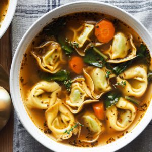 On a cold night, this 30 Minute Healthy Tortellini Soup recipe will be your best friend! Packed with fresh veggies and pasta, it's warming, flavorful, and easy to make. So if you’re craving cosy, nourishing meals right now, you’ll love this tortellini soup. It cooks up in just over 30 minutes, so it’s easy to make on a weeknight. The pillowy, cheesy tortellini makes it filling and fun to eat, i.e. kid-friendly. In this overhead shot the soup is served on a plate and the tortellini can be clearly seen with the chard, carrots and broth. It's topped with a few fresh thyme sprigs and there's a bit of bread on the side. The plate is laying on a tea towel.