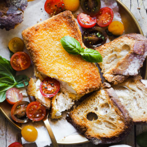 This Pan-Fried Crusted Feta with Cherry Tomatoes is a perfect appetiser that everybody loves. The feta cheese is coated with panko for extra crispiness and is accompanied by a cherry tomato and basil salad that pairs perfectly with the cheese. Serve it with your favourite bread and a little honey to contrast with the salty feta. And voilà, a quick appetiser ready to be devoured! | Paula's Apron Recipe