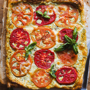 This Cheesy Ricotta Roasted Tomato Tart with Pesto is a true summertime delight that makes everybody always go for seconds (and thirds, fourths...)! Crunchy puff pastry topped with a cheesy pesto layer that irresistibly contrasts both in texture and flavours with the roasted tomato. Plus, baking the tomato enhances its flavours and makes it sweeter, so this tart is a great way to use up any green tomatoes you may have laying around (or it's also a great way to use those not so good looking tomatoes!). | Paula's Apron Recipe
